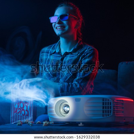 Girl watching a movie. Watching movies in 3D, with glasses. Cinema for home, relaxation and fun. Popcorn. Creative light. Square photo