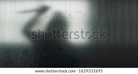 Blurred silhouette of murderer or robber shadow with big knife in hand behind Frosted glass in the bathroom background,concept of scary crime scene of horror or thriller movies,Halloween theme