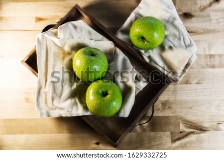 Still life of fruit, with 3 green apples on a wooden tray. Closeup and depth of field