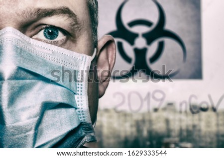 Half of a man's face with a surgical mask in the background "Biohazard sign" (public use) and the inscription "2019-nov" in a dramatic concept