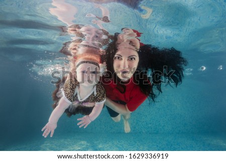 Mom and little daughter dives underwater in the pool. Healthy family lifestyle and children water sports activity. Child development, disease prevention 