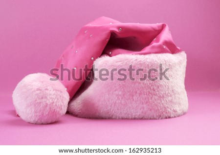 Pretty pink feminine santa hat with festive Christmas decorations on pink background.