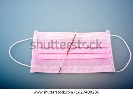 Glass mercury on a pink surgical mask on a blue background