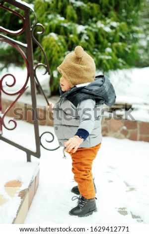 Baby boy in cozy winter clothes trying to make his fisrt steps outside in snowy winter day