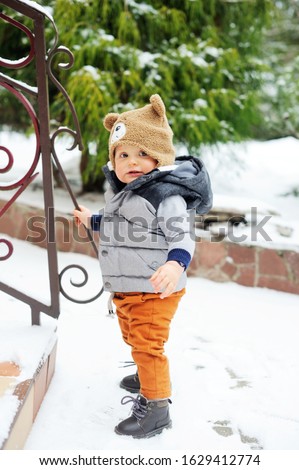 Baby boy in cozy winter clothes trying to make his fisrt steps outside in snowy winter day