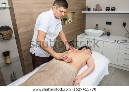young european girl doing back massage, neck, young handsome massage therapist, she is lying on the massage couch