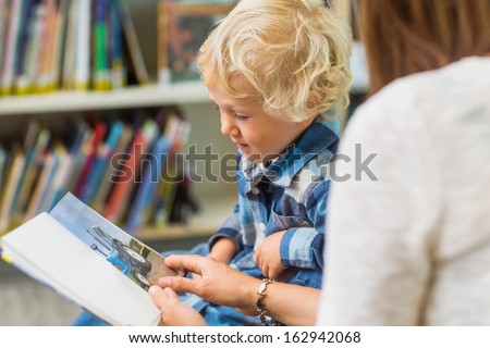 Schoolboy with teacher looking at picture book in library