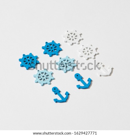 Marine pattern from colorful plastic anchors and steering wheels on a light grey background with shadows, copy space.
