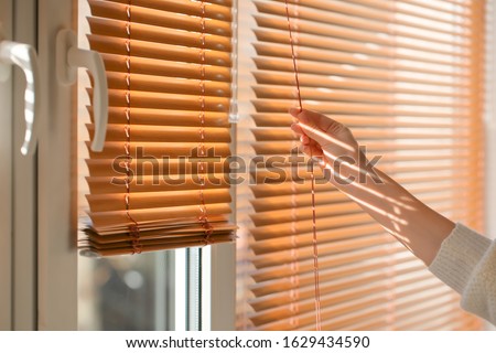 Woman opening blinds on window Royalty-Free Stock Photo #1629434590