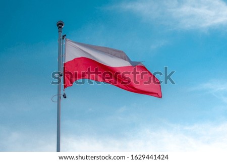Poland flag flies in the wind against a blue clear sky