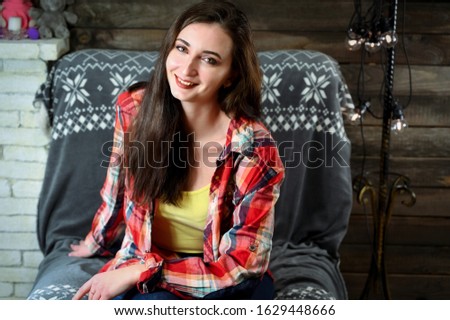 The concept of home comfort. Photo of a pretty young brunette woman with good make-up sits on a sofa in the home interior. Smiling happy.