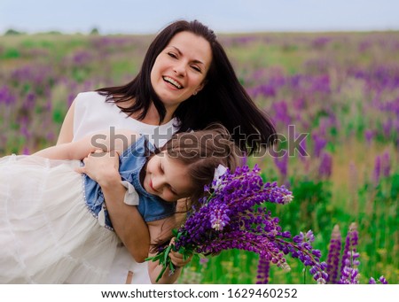 Beautiful mother and daughter in lupine field. Mom is holdind her little daughter in the field with violet flowers. Mother's Day Concept. Blooming Lupine flowers. Happy mom and child girl.