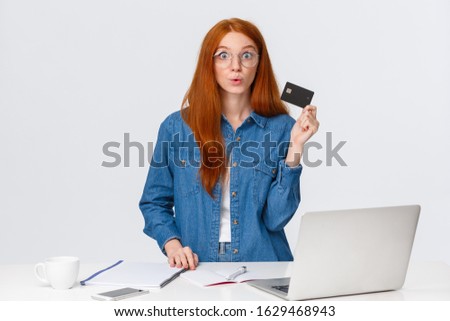 Excited and amused, curious good-looking redhead girl want try cashback online bank offer, holding credit card, folding lips in wow wondered, look camera impressed, stand near laptop