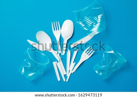 White single-use plastic knives, spoons, forks on a blue background. Say no to single use plastic. Environmental, pollution concept. Royalty-Free Stock Photo #1629473119