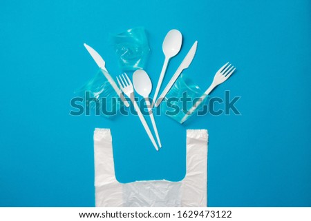 White single-use plastic knives, spoons, forks and bag on a blue background. Say no to single use plastic. Environmental, pollution concept. Royalty-Free Stock Photo #1629473122