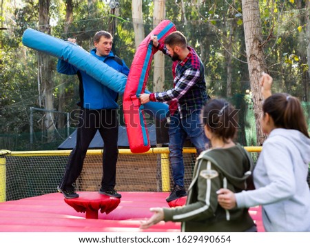 Happy male friends fighting by big stuffed beams at outdoor amusement playground