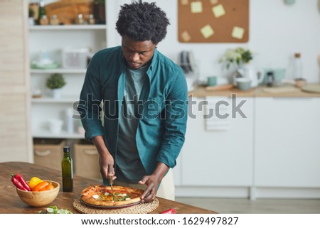 Young African man standing in the kitchen and he is going to eat homemade pizza for lunch