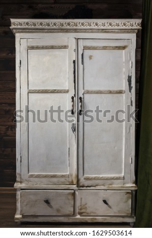 Old painted white cabinet with decorative borders and metal door knobs on dark background. Vintage wooden furniture. Royalty-Free Stock Photo #1629503614