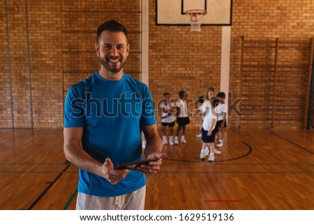 Front view of happy basketball coach using digital tablet at basketball court in school