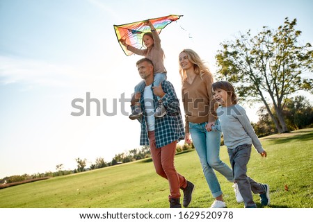 Portrait of cheerful parents with two kids walking with kite in the park on a sunny day. Family, kids and nature concept. Horizontal shot. Front view. Dutch angle Royalty-Free Stock Photo #1629520978