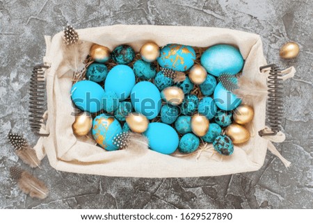 Blue and golden Easter eggs in basket on gray concrete background. Top view, flat lay