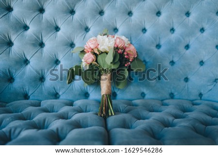 The bride's wedding bouquet of roses and peonies lies on a blue sofa in a beautiful interior. Photography, concept.