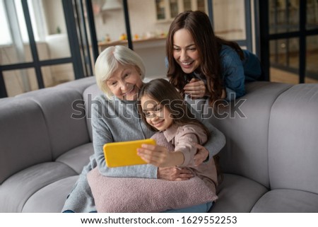 Womans happiness. Happy and smiling little girl her mom and grandmother taking pictures together at home on the couch, in a great mood.
