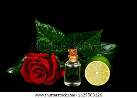 Glass bottle of oil with red rose, limes and green leaves isolated on a black background.