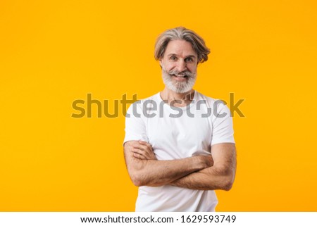 Picture of cheerful positive elderly grey-haired bearded man posing isolated over yellow wall background.