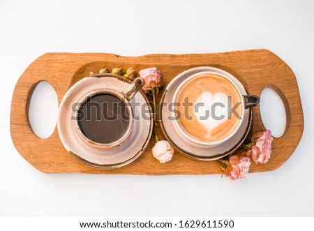 Two cups of coffee decorated with hearts on a wooden tray decorated with roses are on a white table