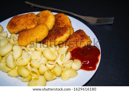 Fried chicken nuggets and boiled pasta with ketchup on a white plate on a dark background. Close up.