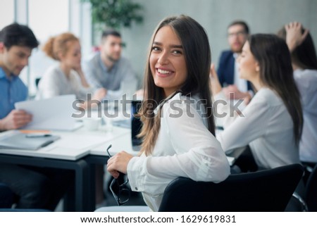 Positive secretary smiling to camera during meeting with colleagues working on background Royalty-Free Stock Photo #1629619831