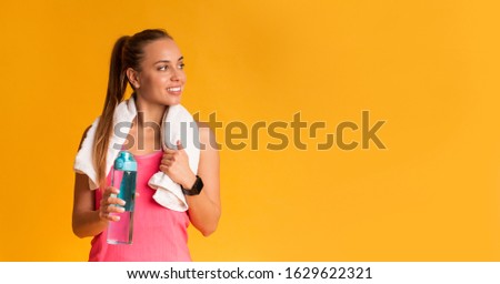 Fitness Concept. Sporty Girl With Bottle Of Water And White Towel Wrapped Around Neck Looking Aside At Copy Space On Yellow Background, Free Space