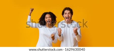 Big Win. Happy interracial couple rejoicing success, celebrating victory with raised fists, exclaiming with joy over yellow background, panorama