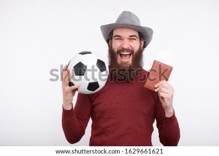 Happy bearded man in casual holding soccer ball and passport with tickets