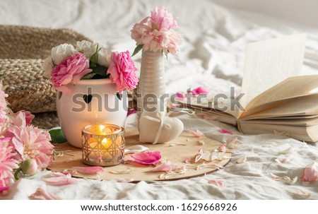 Still life details in home interior of living room. Candle and Vase with roses and peonies flowers and spring decor on the books. Read, Rest. Cozy spring concept.