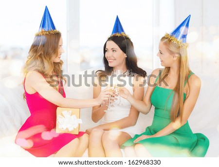 celebration, drinks, friends, bachelorette party, birthday concept - three smiling women wearing blue hats with champagne glasses and gift