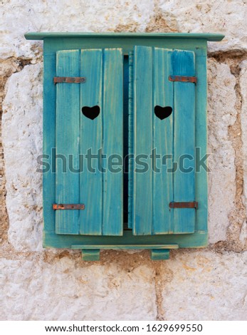 A heart-shaped hole in the picturesque blue wooden shutters on the window of an old stone Croatian house. Romantic picture for Valentine's day, horizontal orientation.