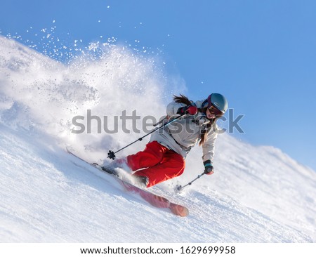 Dynamic picture of a skier on the piste in Alps. Woman skier in the soft snow. Active winter holidays, skiing downhill in sunny day. Ski rides on the track with swirls of fresh snow.