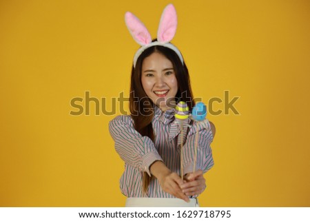 Happy girl with bunny ears and Easter eggs on yellow background.