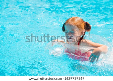 little red-haired girl swims in the summer pool