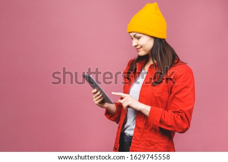 Portrait of a smiling young woman using tablet computer isolated on a pink background.