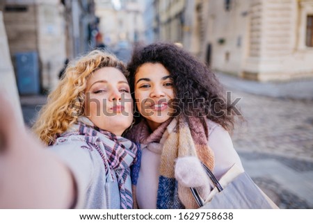 Two attractive smiling young curly blond and brunette women best frieds making funny faces for selfie photo after shopping in the city. Consumerism, shopping,lifestyle concept.