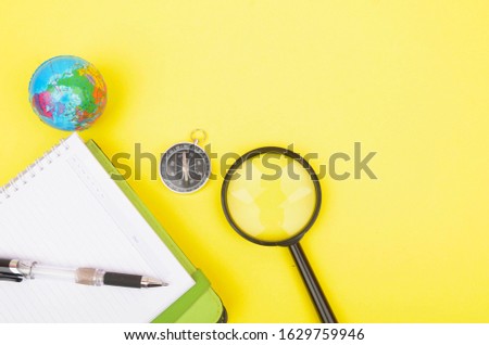 conceptual image. Notebook, compass, magnifying glass, pen and world globe on yellow background.