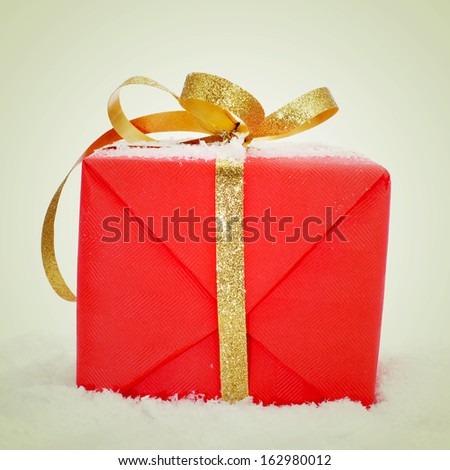 picture of a gift wrapped with red wrapping paper and with a golden ribbon on the snow, with a retro effect
