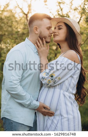 Fashionable and stylish happy pregnant woman and her husband dressed a pastel white and blue tone in the garden on the sunset