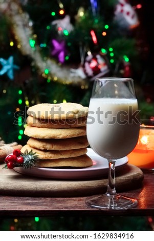 Cookies biscuits for Santa Claus near a christmas tree decorated with flashing lights,mistletoe and a glass of milk on a wooden tray, atmospheric Christmas picture