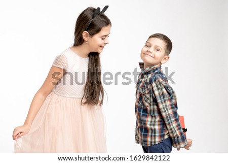Attractive brunette girl in beige dress and with black ears on her head, sister waiting for a present, her brother in shirt holds a gift box in hands behinde his back. St. valentine's day, Woman's day