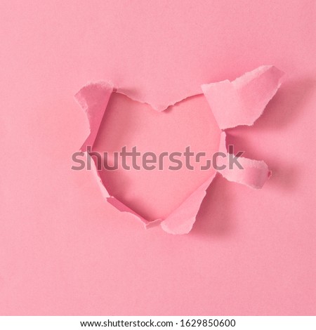 Torn paper hole in heart shape. Pink paper background Valentines day concept