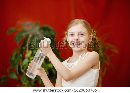 cute pretty blonde girl of 8 years old, spraying water from a spray bottle, moisturizing the air, caring for domestic plants, red background